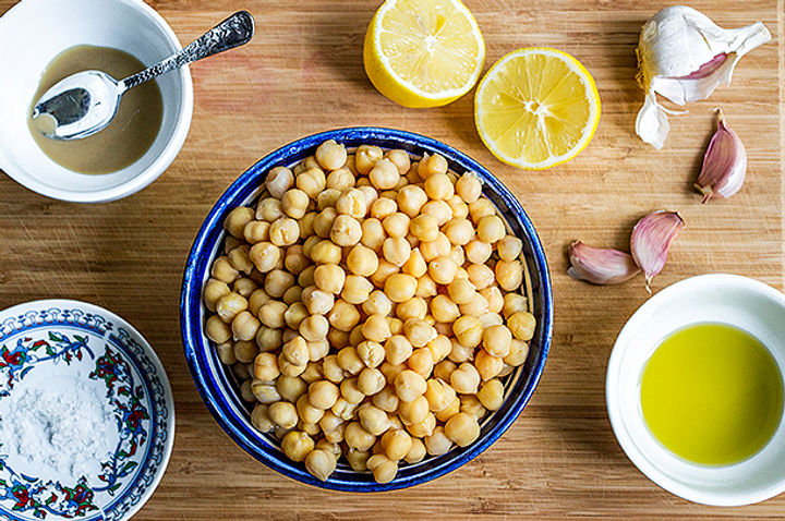 Image of ingredients for humous including a bowl of chickpeas, some lemons, garlic and tahini 