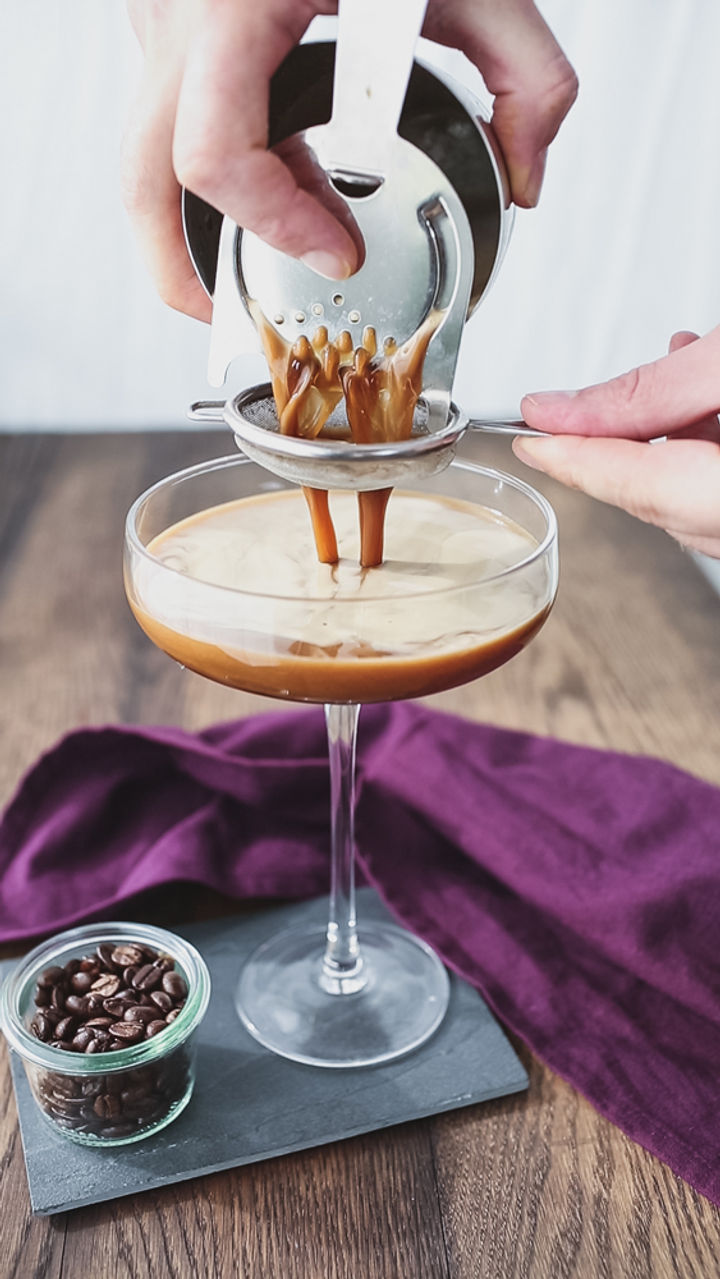 Image of shaken espresso martini being drained from a cocktail shaker into a glass
