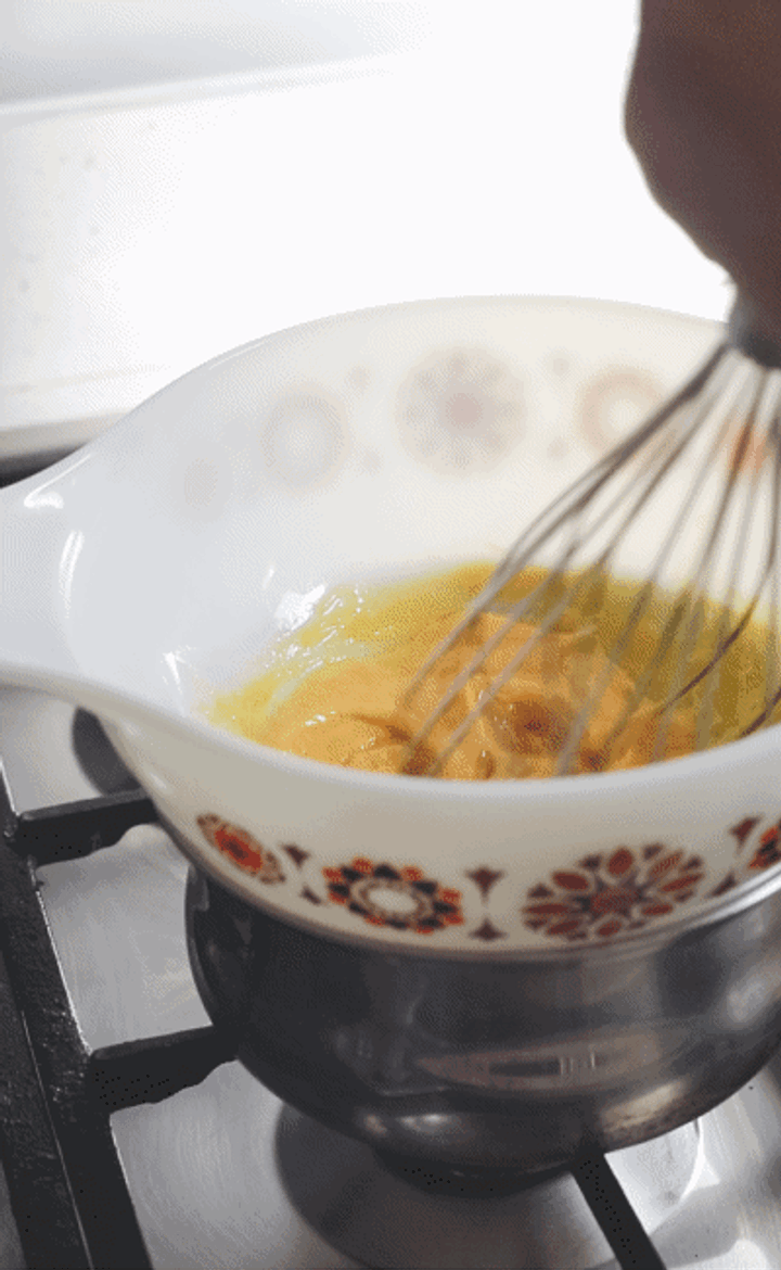 GIF of butter being slowly whisked into egg mixture in a bowl over a pan of boiling water