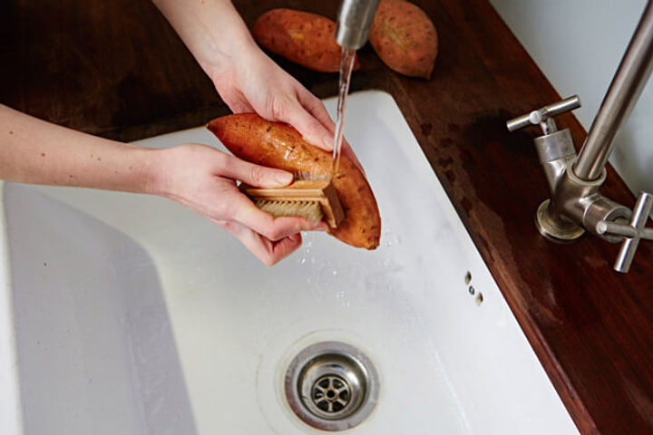 Image of sweet potato being scrubbed over a sink