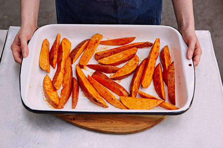 Image of chopped, raw sweet potato wedges on a tray ready to cook