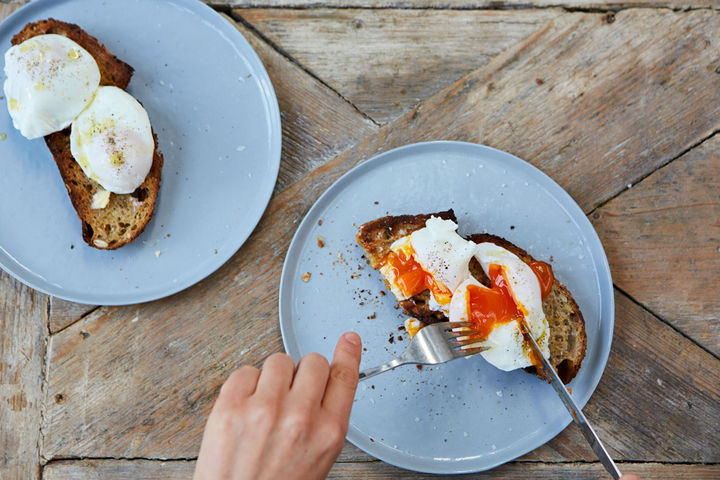 Image of poached egg on toast being cut open with a knife and fork
