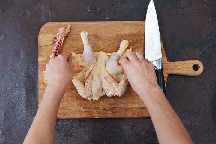 Image of raw, whole chicken being spread on a chopping board
