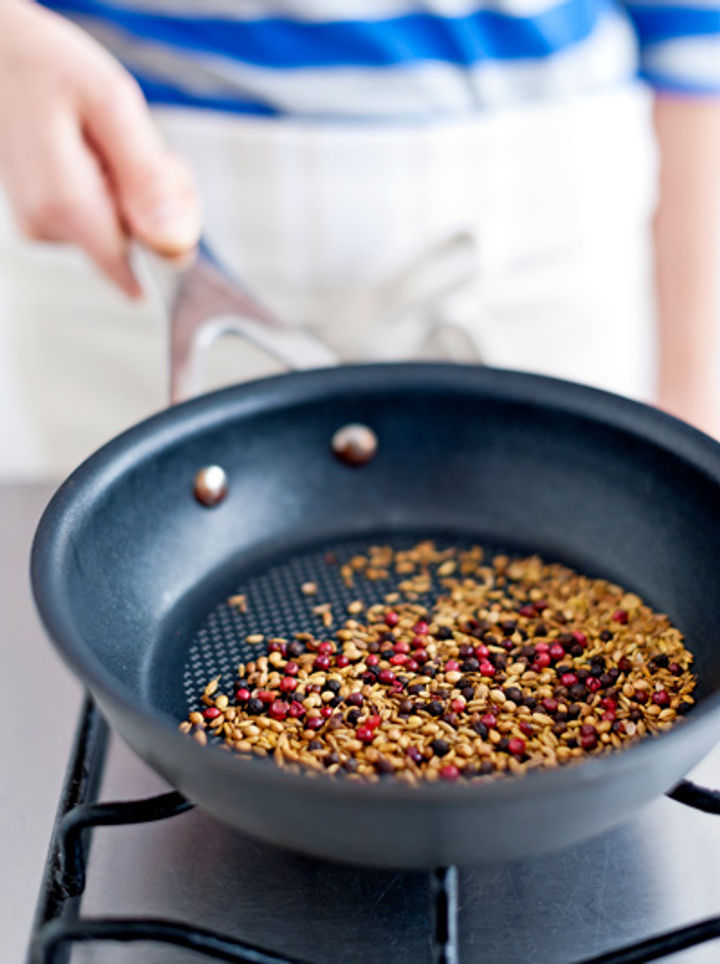 Image of peppercorns, fennel and coriander seeds being dry toasted in a pan