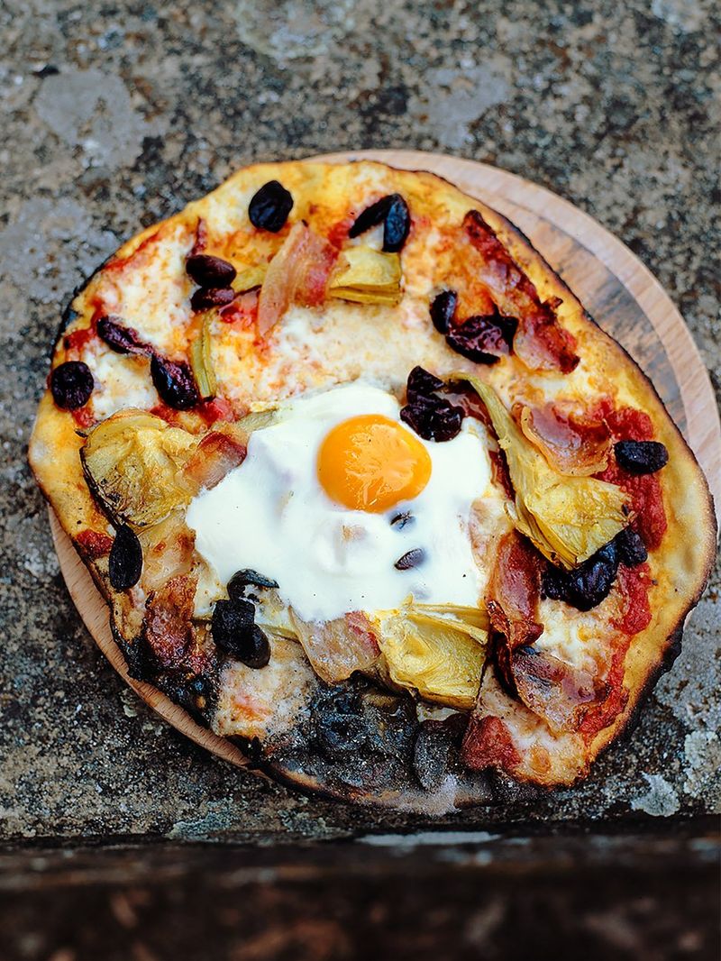 Pizza mit ei, prosciutto, artischocken, oliven, mozzarella, tomatensauce und basilikum