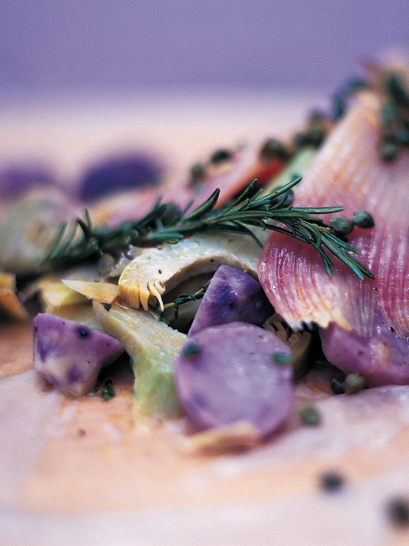 Rochenflügel mit artischocken, violetten kartoffeln und kapern in der papierhülle gegart