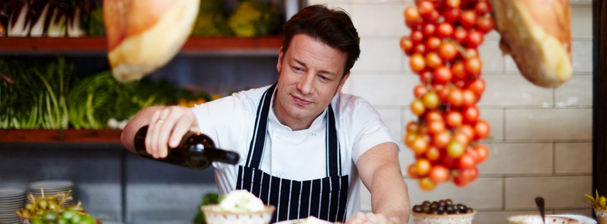 Jamie Oliver in the kitchen drizzling oil over buratta on an antipasti plank